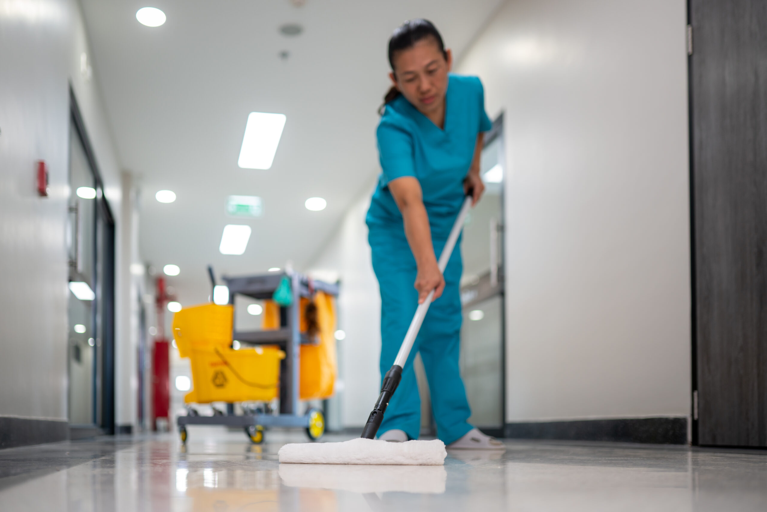 A woman in a blue scrub suit is mopping a floor A woman in a blue scrub suit is mopping a floor. Concept of cleanliness and orderliness